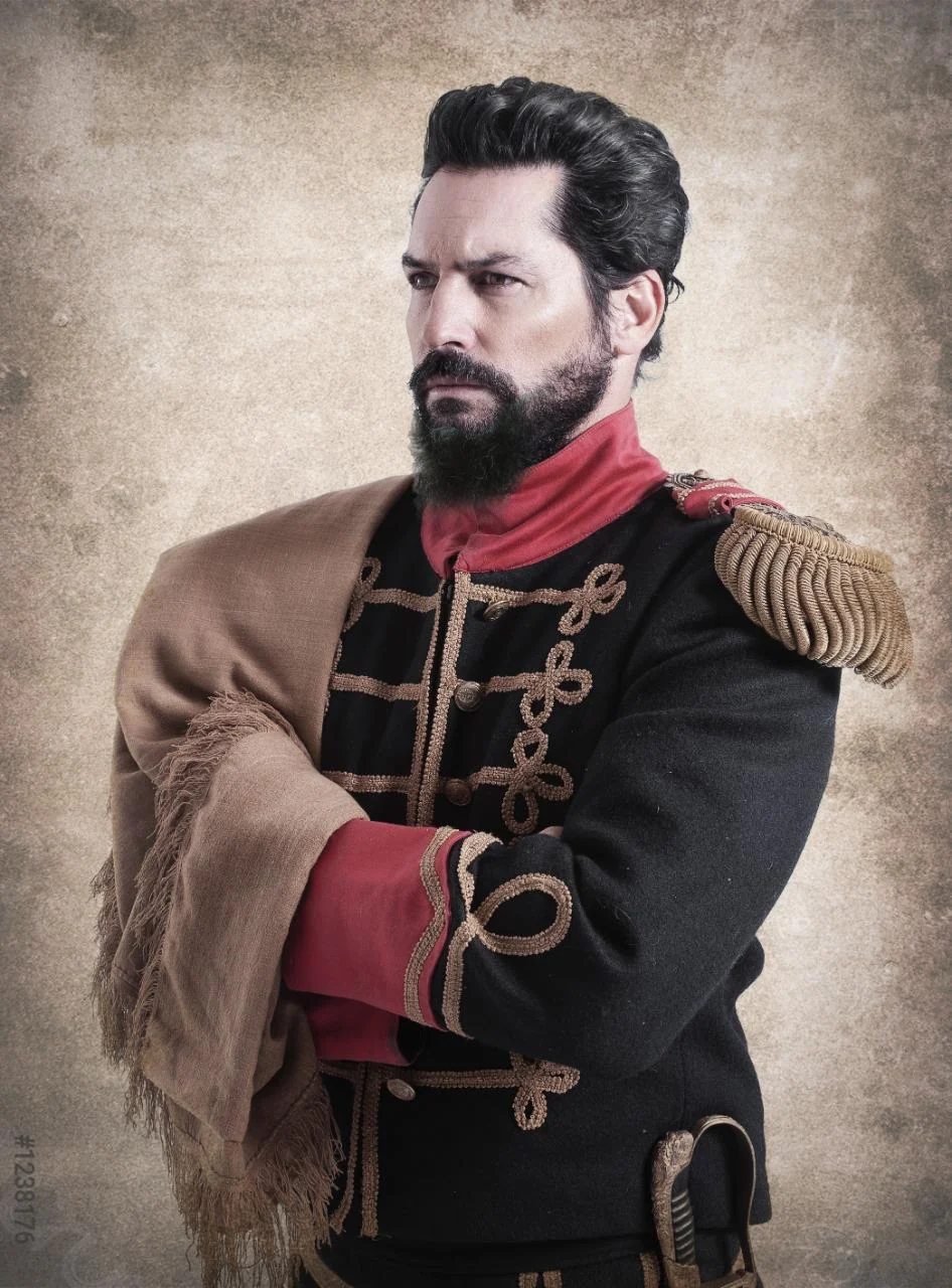 Nacho Valenti Lacroix as General Güemes in a black uniform with red collar and cuffs and gold braid, arms crossed